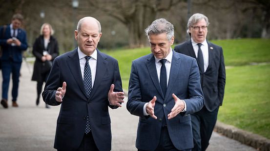 Kanzler Scholz und Ministerpräsident Golob laufen im Grünen nebeneinander. Beide gestikulieren.