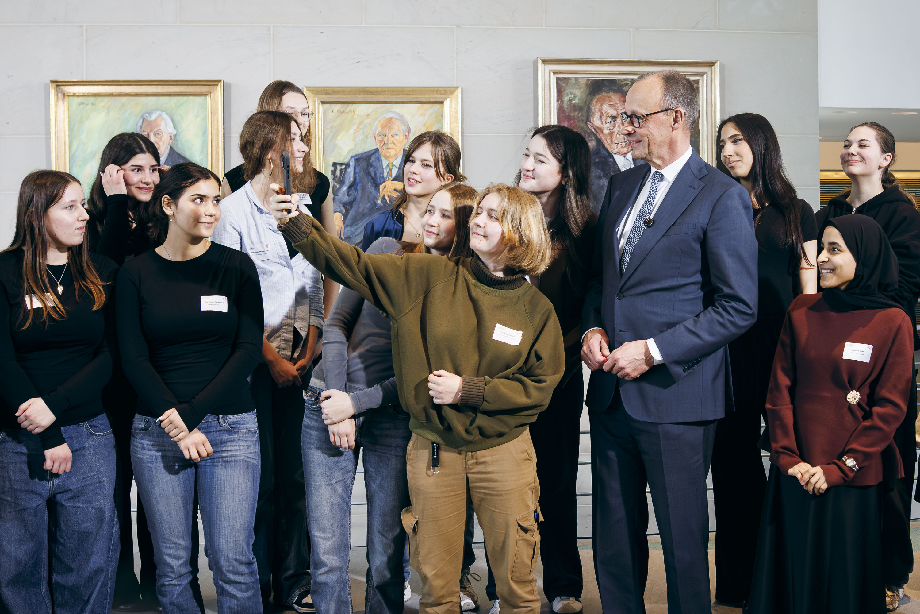 Bundeskanzler in einer Gruppe von Schülerinnen im Bundeskanzleramt. Eine Schülerin nimmt mit ihrem Handy ein Selfie der Gruppe auf.