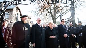Die Kanzlerin steht unter dem Tor zum ehemaligen Konzentrationslager Auschwitz mit dem Schritzug "Arbeit macht frei"