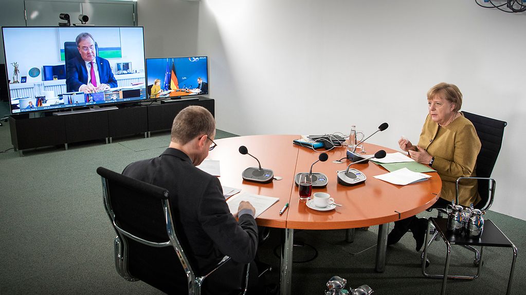 Chancellor Angela Merkel and Berlin's Governing Mayor attend the video conference in the Federal Chancellery. In the background Armin Laschet can be seen on a screen.