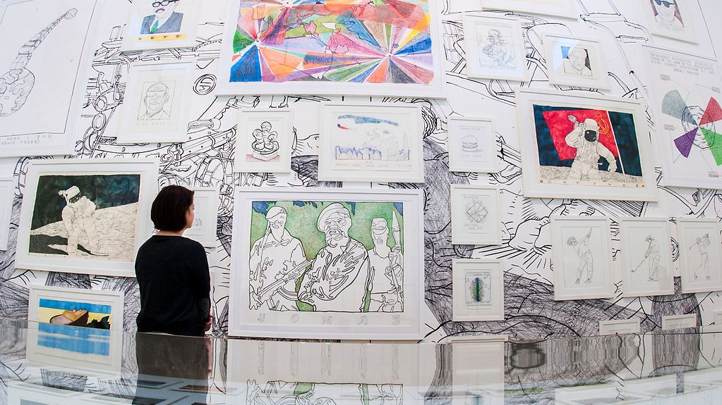 Eine Besucherin steht bei der Biennale in Berlin vor Bildern des Künstlers Tonel.
