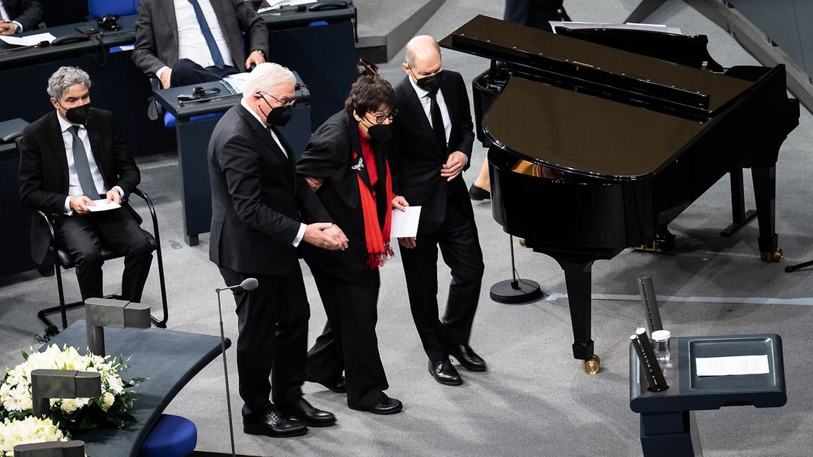 Das Bild zeigt, wie Bundespräsident Steinmeier und Kanzler Scholz, Inge Auerbacher zum Rednerpult geleiten.