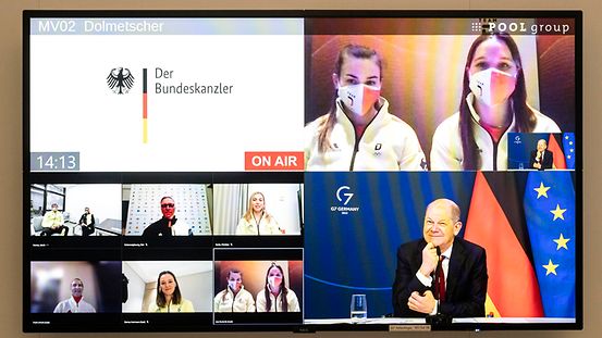 Das Foto zeigt einen Bildschirm mit einem Bild des Bundeskanzlers und der Sportlerinnen und Sportlern. 