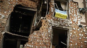 Eine zerstörter Häuserfassade in Irpin. In der Mitte hängt eine Ukraine-Flagge.
