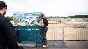 Bauarbeiter stellen eine Informationstafel im Vorfeld der Grundsteinlegung des Batteriezelwerks von VW in Salzgitter auf.