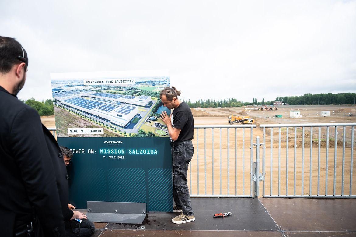 Bauarbeiter stellen eine Informationstafel im Vorfeld der Grundsteinlegung des Batteriezelwerks von VW in Salzgitter auf.