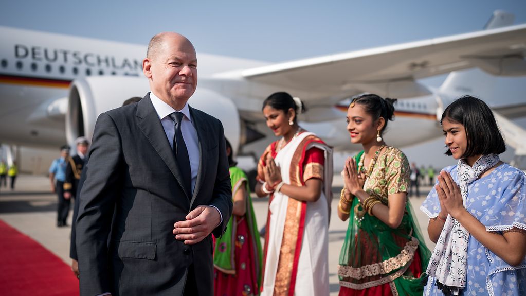 Bundeskanzler Scholz steigt in Neu-Delhi aus dem Regierungsflugzeug aus und läuft auf dem roten Teppich an indischen Frauen in traditioneller Kleidung vorbei.