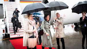Nancy Faeser, Bundesministerin des Inneren und für Heimat, und Annalena Baerbock, Bundesministerin des Auswärtigen, unter Regenschirmen auf dem Flughafen in Tokio.