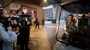 Bundeskanzler Olaf Scholz sitzt beim G20-Gipfel in einem kleinen Auto, Kameramänner filmen ihn bei der Abfahrt.