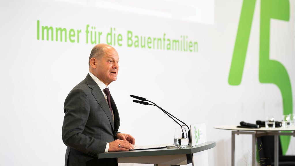 Kanzler Scholz am Rednerpult hinter ihm das Logo zum 75. Jubiläum des Bauernverbandes samt Aufschrift "Immer für die Bauernfamilien".