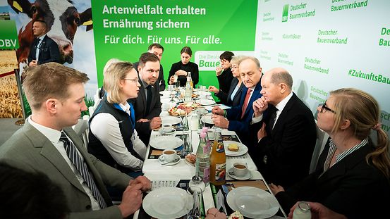 Bundeskanzler Scholz sitzt am Tisch mit jungen Bäuerinnen und Bauern.