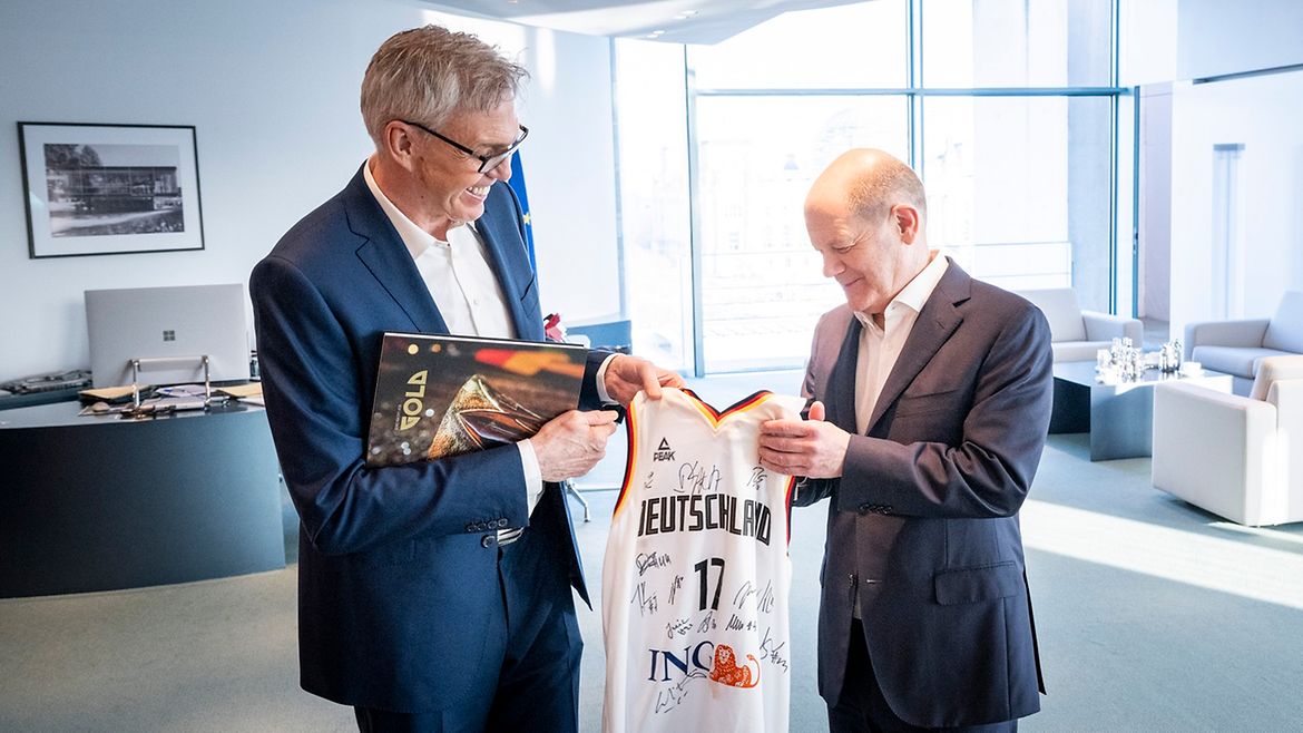 Basketball-Nationaltrainer Gordon Herbert (l.) überreicht Bundeskanzler Scholz ein unterschriebenes Basketball-Trikot.