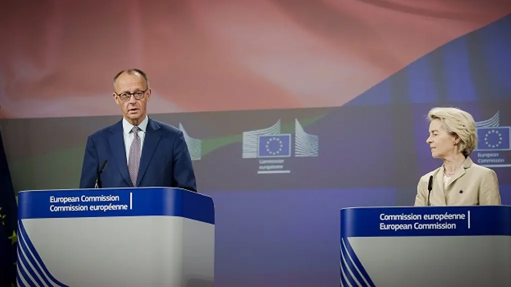 Bundeskanzler Merz und Kommissionspräsidenten von der Leyen lächeln sich gegenseitig vor der europäischer und deutscher Flagge an.