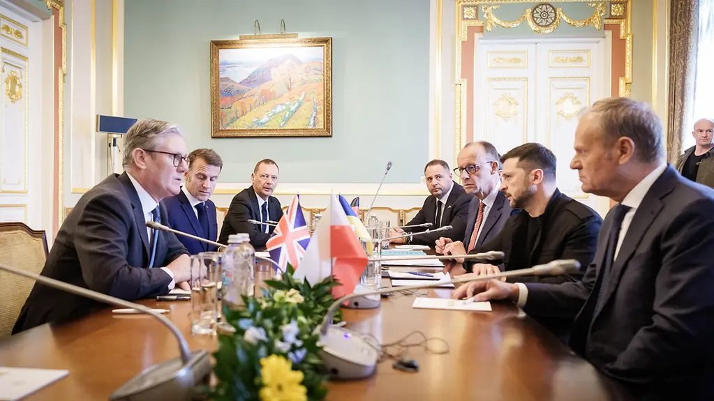 Merz, Macron, Starmer Tusk und Selenskyj sitzen an einem Tisch in einem prunkvollen Besprechungssaal. 