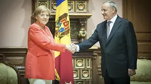 President Nicolae Timofti welcomes the Chancellor in front of a Moldovan flag.
