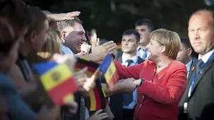 Angela Merkel shakes hands with members of the crowd who have come with flags to welcome her.