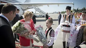 Chancellor Angela Merkel is welcomed at the airport and presented with a bouquet.
