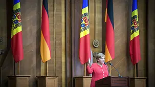 Angela Merkel speaks in front of a bank of flags.