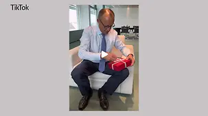 Das Bildschirmfoto zeigt Bundeskanzler Merz mit einem roten Geschenk in der Hand in seinem Büro im Bundeskanzleramt.