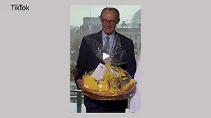 Das Bildschirmfoto zeigt Bundeskanzler Merz mit einem Brot-Präsentkorb in der Hand im Bundeskanzleramt.