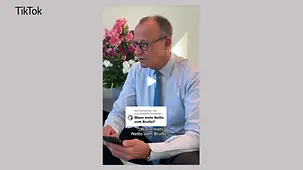 Bundeskanzler Merz mit einem Smartphone.