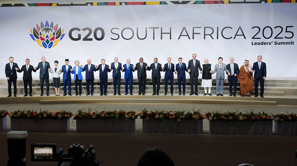 Das Foto zeigt Staats- und Regierungschefinnen und -chefs beim G20-Treffen in Südafrika auf einer Bühne, sich an den Händen haltend.
