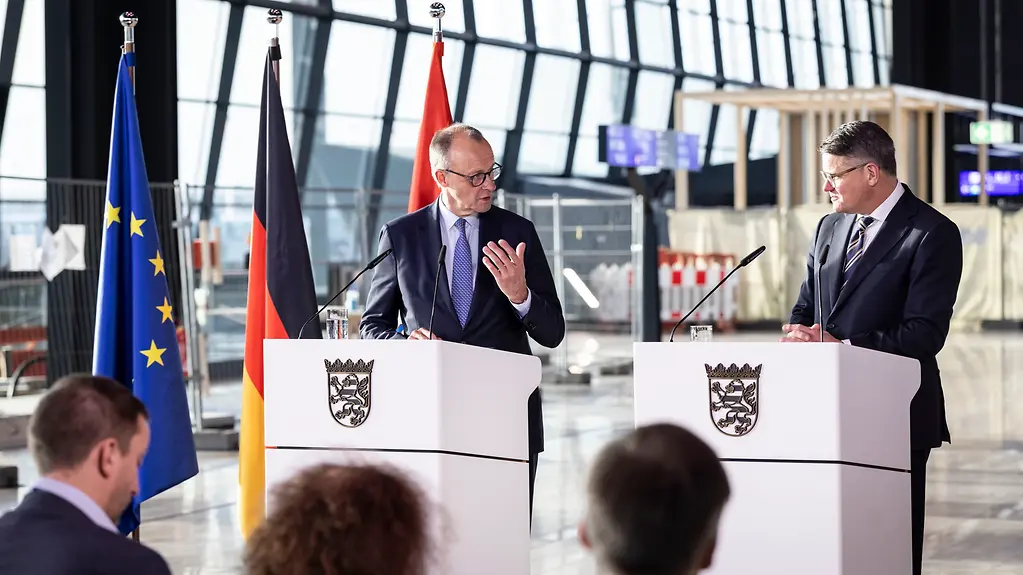 Das Foto zeigt Kanzler Merz und Hessens Ministerpräsident Boris Rhein bei einem Pressestatement am Flughafen Frankfurt.