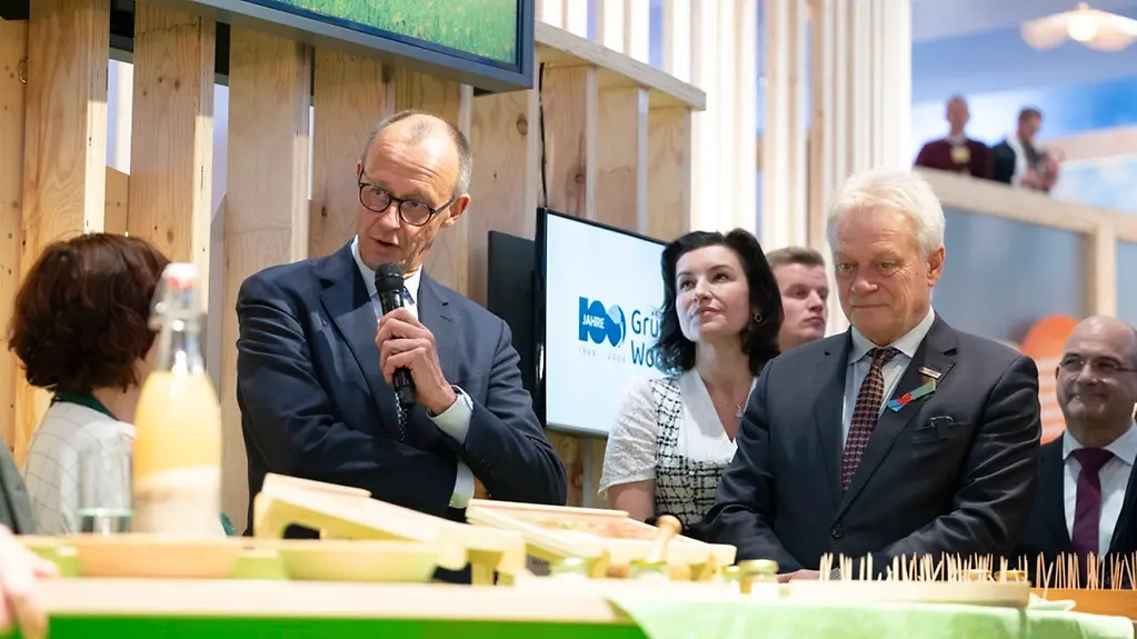 Bundeskanzler Merz hält ein Mikrofon in der Hand, im Hintergrund Landwirtschaftsminister Rainer und Forschungsministerin Bär.