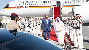 The photo shows Federal Chancellor Friedrich Merz being received on a tarmac in Qatar. The government plane is visible in the background.