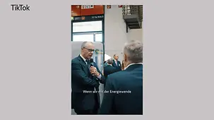 Bundeskanzler Merz auf der Internationalen Handwerksmesse im Austausch mit Ausstellern. In der Hand hält er ein Mikrophon.