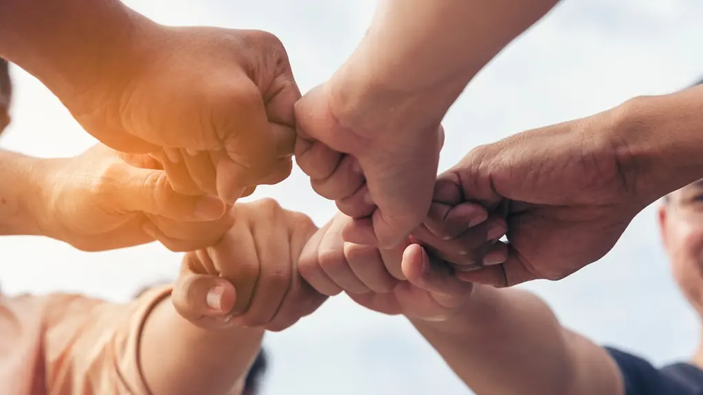 Nahaufnahme von Händen von Menschen unterschiedlicher Herkunft, die im Kreis stehen und sich die Hände reichen.