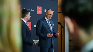 Kanzler Merz am Mikrofon, vor einer Standwand mit Aufschrift Hannover Messe.