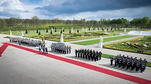 Der Bundeskanzler und der brasilianische Präsident inspizieren auf einem roten Teppich die Ehrenwache der Bundeswehr. Im Hintergrund der Schlossgarten von Schloss Herrenhausen.