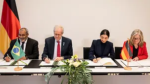 Ministerin Alabali Radovan unterschreibt eine Partnerschaft. Neben ihr sitzen der brasilianische Umweltminister und zwei weitere Personen, die ebenfalls Schriftstücke unterschreiben.