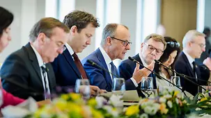 Kanzler Merz spricht in ein Mikrophon, neben ihm sitzen Ministerinnen und Minister der deutschen Bundesregierung.