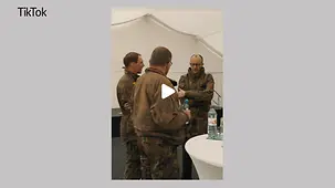Kanzler Merz in Tarnkleidung im Gespräch mit zwei Soldaten.