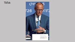 Kanzler Merz auf einer Bühne hinter einem Mikrophon. Vor ihm ein Schild mit der Aufschrift "Deutschland - Land der Ideen".