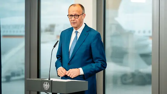Kanzler Merz am Redepult am Flughafen BER