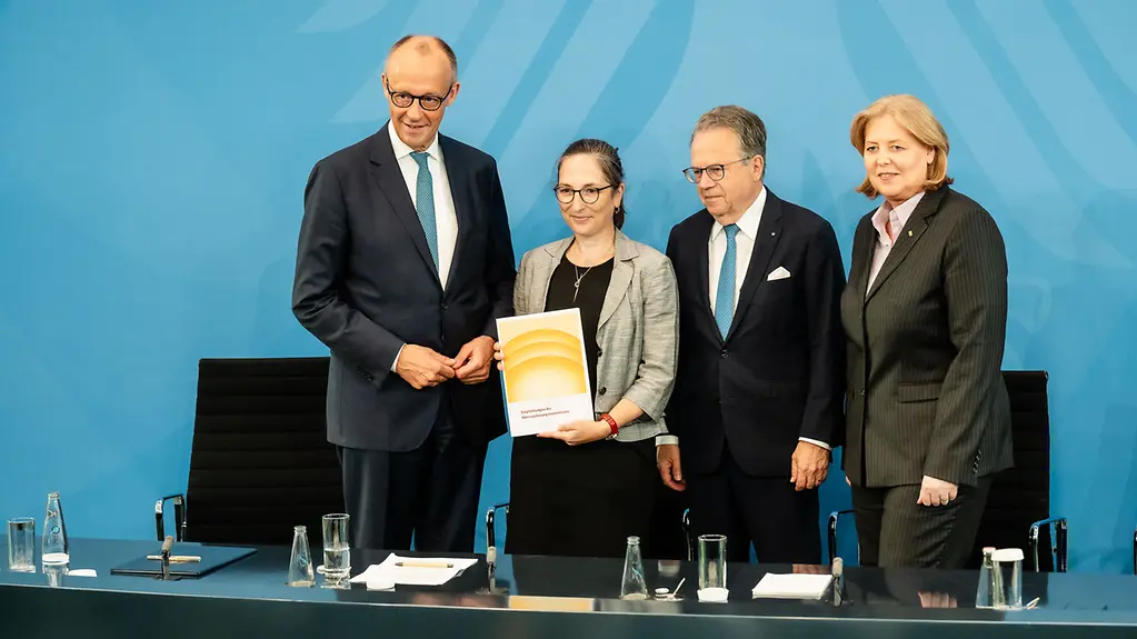Bundeskanzler Merz und Ministerin Bas stehen mit Frank-Jürgen Weise und Constanze Janda in der Regierungspressekonferenz und halten den Bericht der Alterssicherungskommission in den Händen.