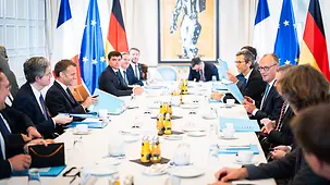 Die deutsche und die französische Delegation an einem langen Besprechungstisch.