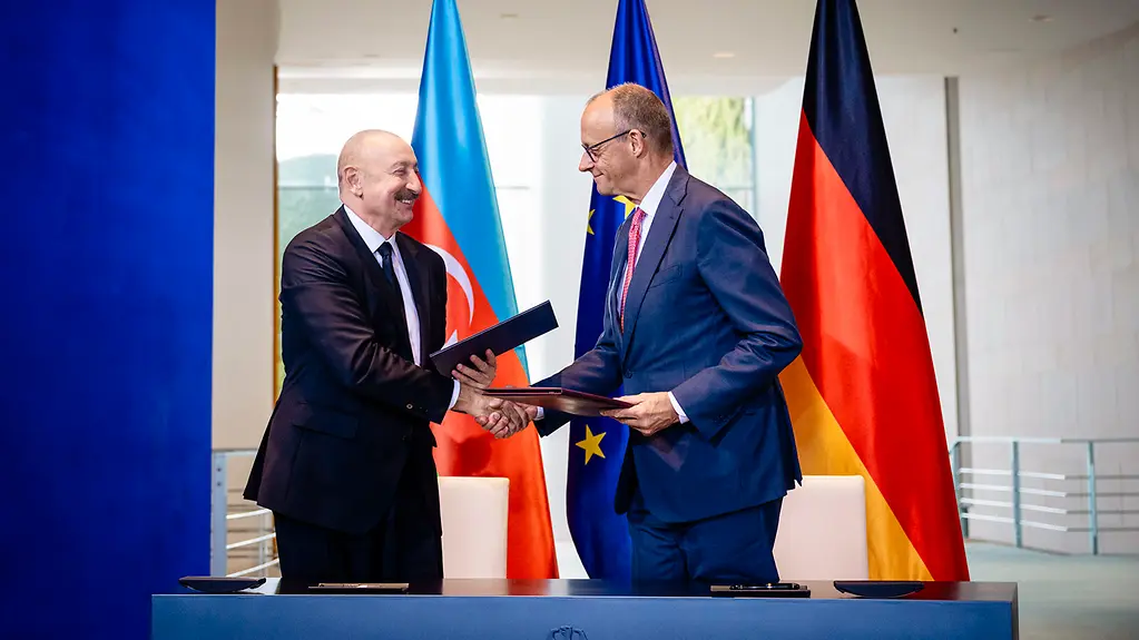 Bundeskanzler Merz und Präsident Alijew beim Handshake, in den Händen halten sie unterzeichnete Dokumente.