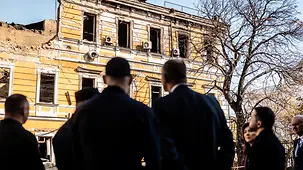 Bundeskanzler Merz zusammen mit Präsident Selenskyj vor einem zerstörten Haus.