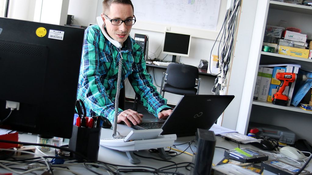 Ein Mann arbeitet an einem Schreibtisch mit vielen Computern.