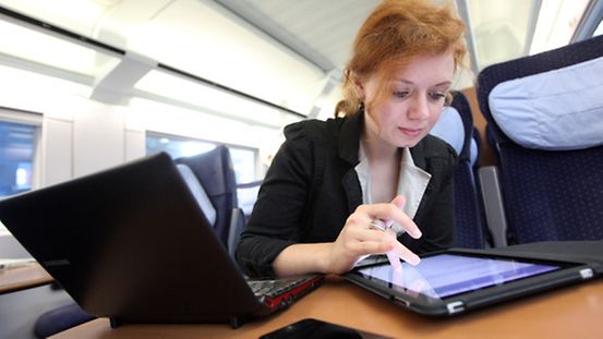 Eine junge Frau sitzt in einem ICE an einem Tisch und arbeitet mit ihrem Laptop