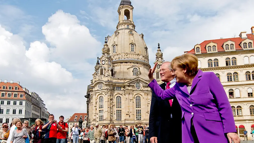 Chancellor Angela Merkel waves to the crowds in Dresden; behind her the celebrated Frauenkirche.