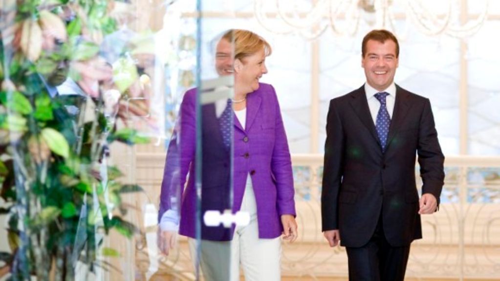 Chancellor Angela Merkel and Russian President Dmitry Medvedev walk towards the camera and smile at one another