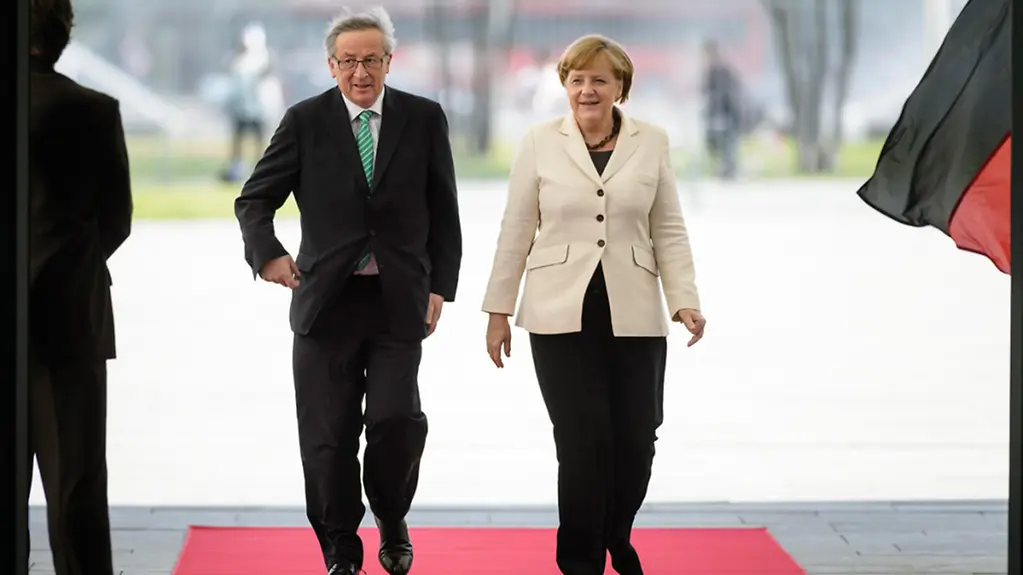 Angela Merkel and Jean-Claude Juncker walk along the red carpet.
