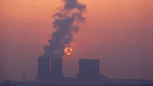 Clouds of steam billow from the cooling tower of the Lippendorf power station silhouetted agains the setting sun.