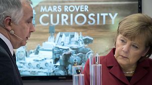 Angela Merkel sands in front of a photo of the Mars Rover.